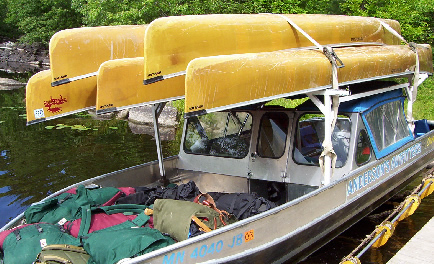 photo of a boat shuttle with five canoes loaded on top